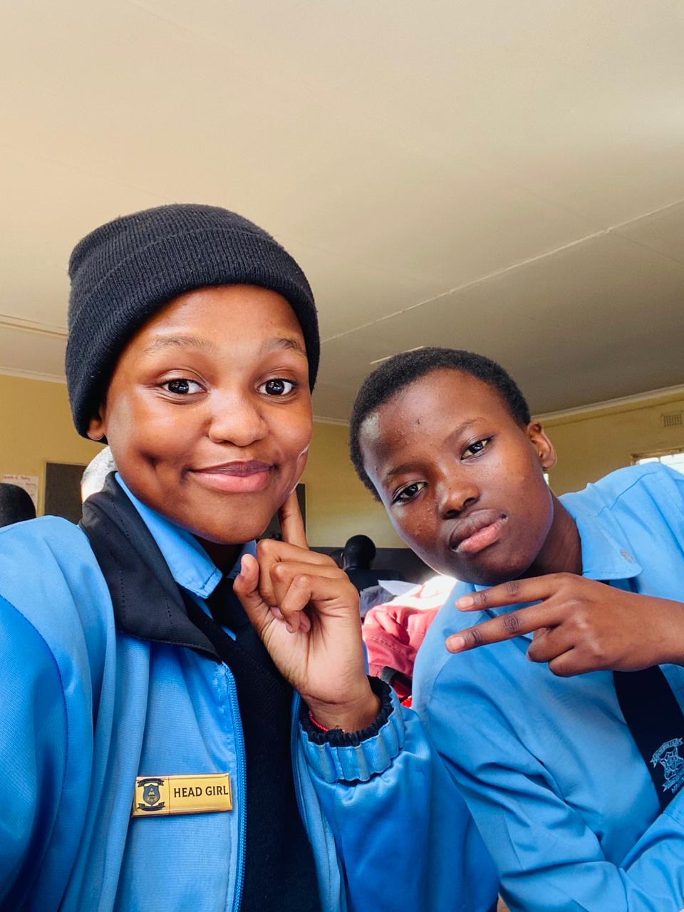 Two learners in blue blazers, one with a Head Girl badge and beanie